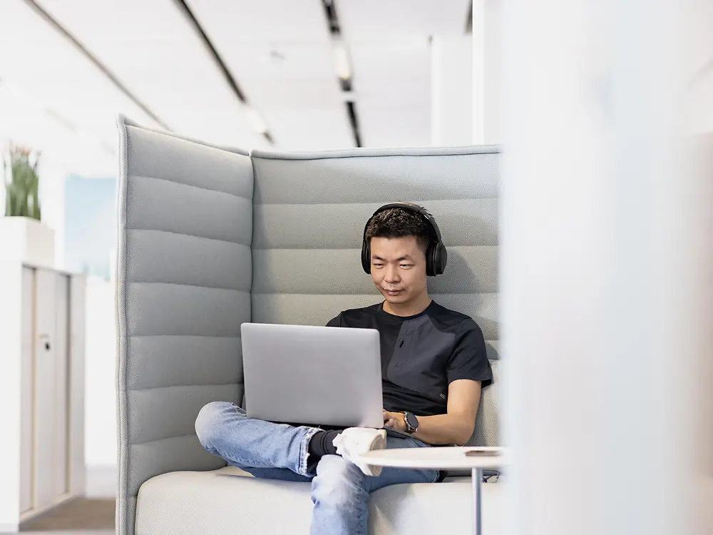 Zamestnanec spoločnosti Henkel so slúchadlami na hlave sústredene pracuje s laptopom.