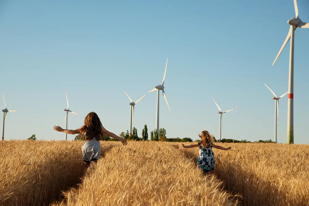 Dievčatá bežia cez pole smerom k veterným turbínam