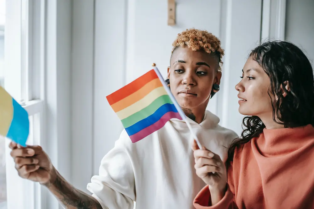 Dve ženy sa rozprávajú a v rukách držia dúhovú vlajku LGBTQ+.
