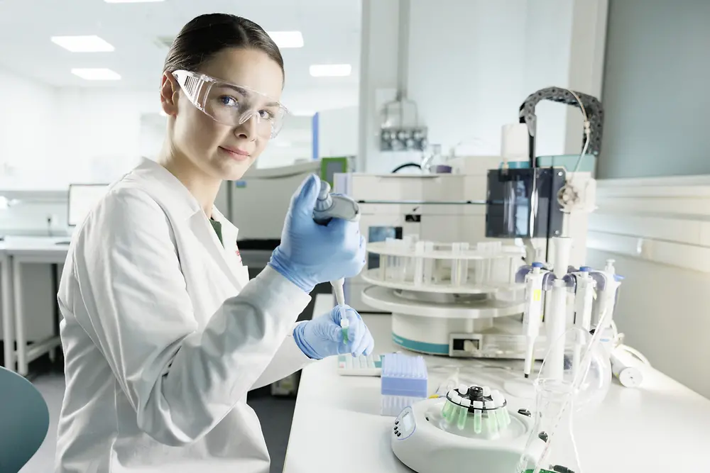 Vedkyňa oblečená v bielom plášti a s ochrannými okuliarmi experimentuje v laboratóriu.