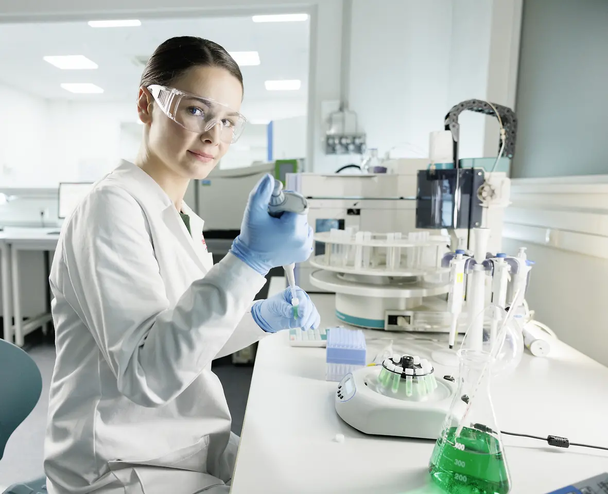 Vedkyňa oblečená v bielom plášti a s ochrannými okuliarmi experimentuje v laboratóriu.