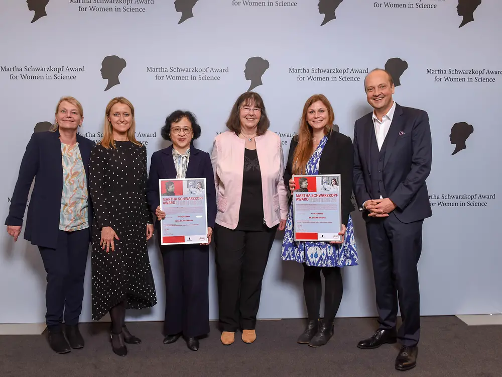 Four Henkel representatives and the two winners of the Martha Schwarzkopf Award are standing next to each other in front of the photo wall. 
