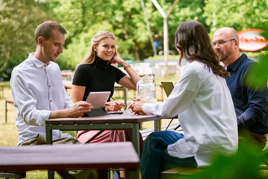 Skupina kolegov sedí spolu vonku a diskutuje o práci s tabletmi a notebookmi, čo predstavuje spoluprácu a otvorenú kultúru zameranú na tím v spoločnosti Henkel.