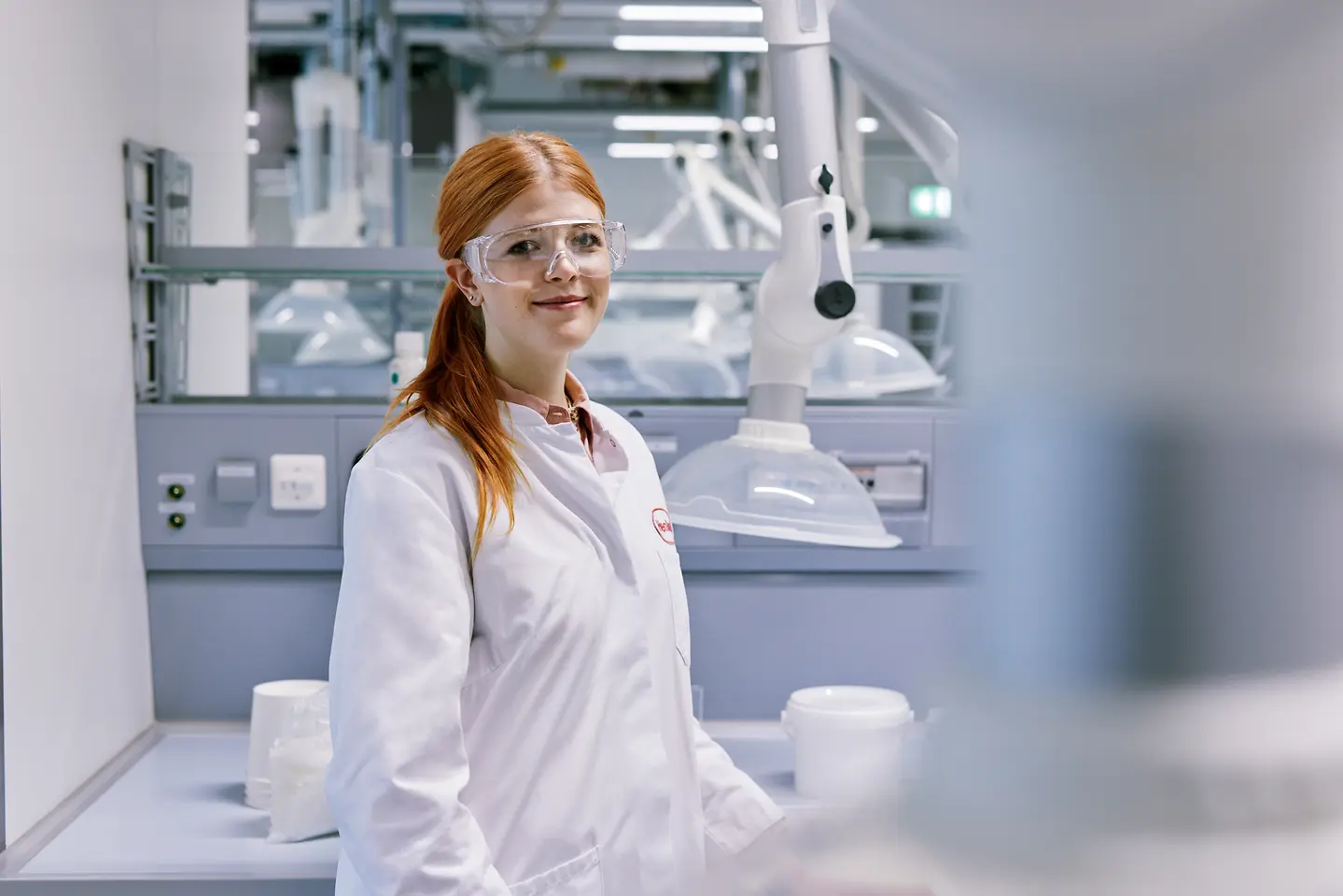 Absolvent začínajúci kariéru v spoločnosti Henkel, oblečený v bielom laboratórnom plášti a stojaci v modernom laboratórnom prostredí s technickým vybavením v pozadí.