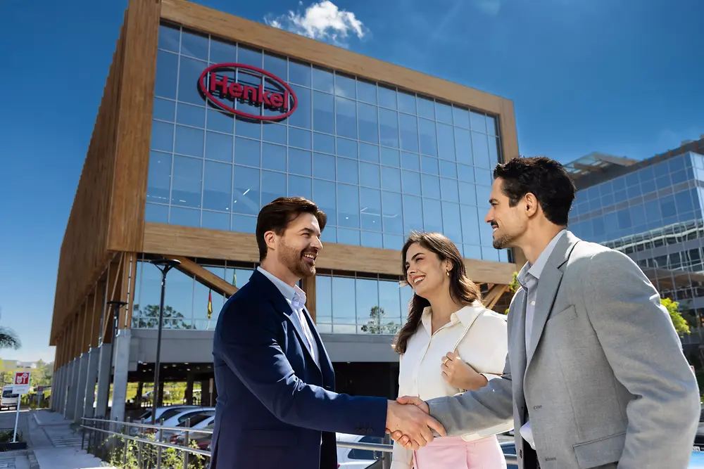 Three people in business attire chat and shake hands outside the Inspiration Center Jundiaí, a modern glass building with a wooden frame and 