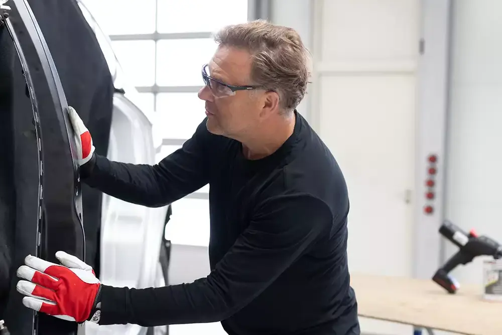 Technik opravujúci alebo servisujúci dvere vozidla v automobilovej dielni.